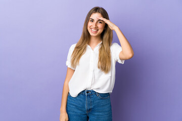 Young woman over isolated purple background saluting with hand with happy expression