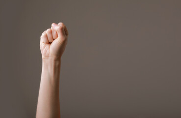 female hand clenched into a fist on a gray background. gesture of fighting, winning or protest....