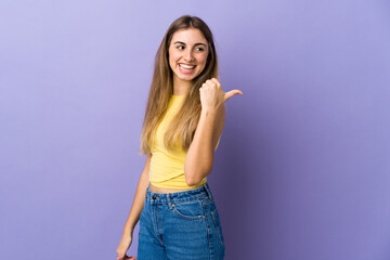 Young woman over isolated purple background pointing to the side to present a product