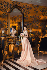 A beautiful young girl in a powdery wedding dress on the background of the interiors of a luxurious historical apartment. An elegant and stylish bride's morning.