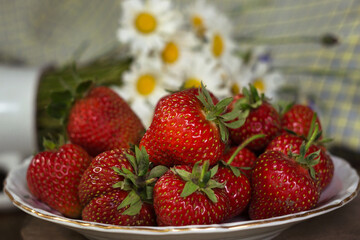 Ripe strawberries in a white old plate, near a rose. Brown wooden background
