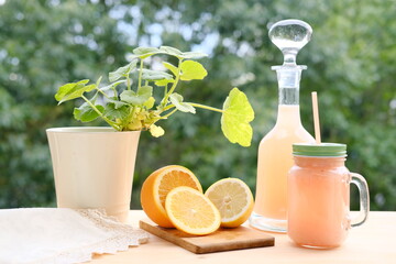 fresh fruit smoothies in a decanter and a mug on a background of green garden foliage, orange...
