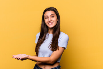 Young Indian woman isolated on yellow background holding a copy space on a palm.