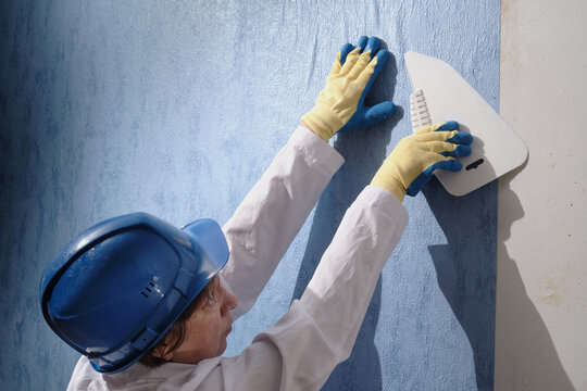 woman, a brunette adult in a white uniform in the process of pasting wallpaper on the wall in an ordinary city apartment, the last stage in the process of repair and construction finishing work