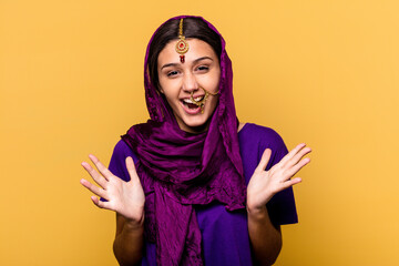 Young Indian woman wearing a traditional sari clothes isolated on yellow background celebrating a victory or success, he is surprised and shocked.