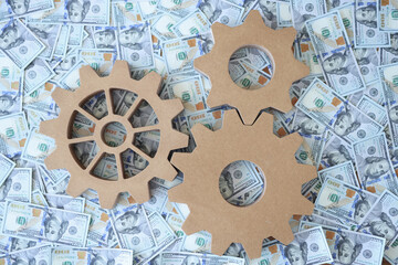Wooden gears lying on lot of dollar bills