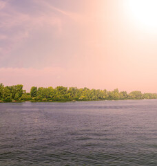 The orange sun shines over the forest and the river. Scenery