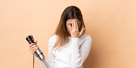 Woman using hand blender over isolated background with tired and sick expression