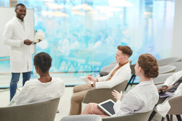 Obraz premium Group of young people wearing lab coats and listening to professor during medical seminar in coworking center, copy space