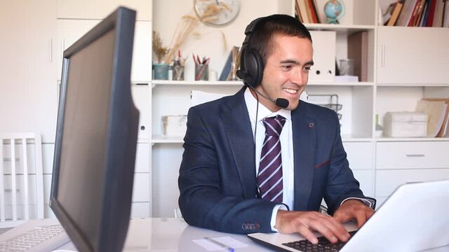 Office worker man is working at computer and talking by headset with client in the office