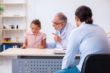 Obraz premium Small girl with her father visiting old male doctor