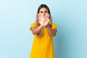 Young hispanic woman over isolated blue background making stop gesture with her hand to stop an act