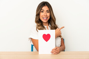 Young caucasian woman holding a valentines day card isolated smiling and pointing aside, showing something at blank space.