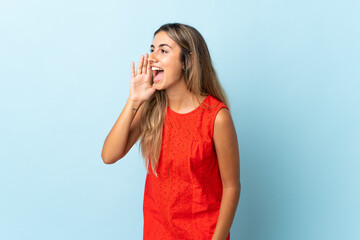 Young hispanic woman over isolated blue background shouting with mouth wide open to the side