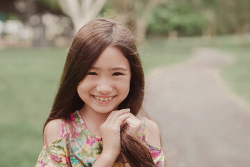 Close up urban lifestyle portrait of a confident, charming and gorgeous mixed race child face, happy multicultural Asian girl in park