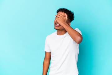Young african american curly man isolated on blue covers eyes with hands, smiles broadly waiting for a surprise.