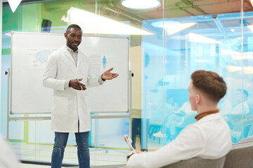 Fototapeta premium Portrait of African-American man standing by whiteboard while giving presentation during medical seminar in college, copy space