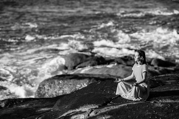 Yoga woman on rocks meditating on the the sea beach. Black and white photo.