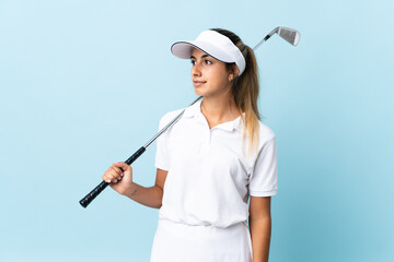 Young hispanic golfer woman over isolated blue wall looking to the side