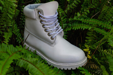 White boot shoe with low platform sole in the foreground, surrounded by green grass