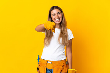Young hispanic electrician woman over isolated yellow wall surprised and pointing front