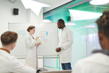 Side view portrait of young woman standing by whiteboard while giving presentation during medical seminar in college, copy space