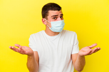 Young caucasian man wearing a protection for coronavirus isolated on yellow background doubting and...