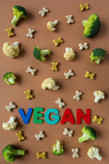 Pattern of Vegetarian dog biscuit in shape of bones with broccoli and cauliflower on beige background with multicolored Lettering VEGAN