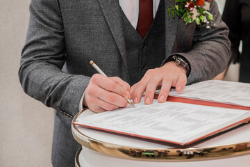 The groom's hands are signed with a pen in the document on the confirmation of the marriage close-up
