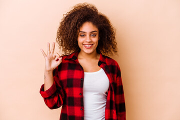 Young african american woman isolated on beige background cheerful and confident showing ok gesture.