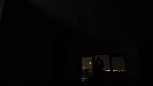 Young couple silhouette hugging indoors in front of window at night. High quality 4k footage