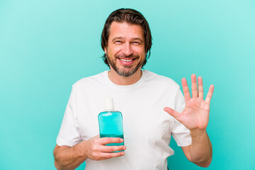 Middle age dutch man sitting holding a mouthwash isolated on blue background smiling cheerful showing number five with fingers.