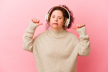 Woman with Down syndrome with headphones isolated on pink background feels proud and self...