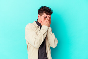 Fototapeta na wymiar Young caucasian man isolated on blue background blink through fingers frightened and nervous.