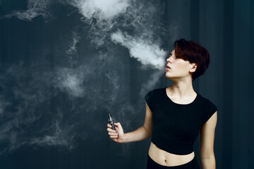 young girl smokes electronic cigarette. The model vaping a vaporizer in the studio.The face of...