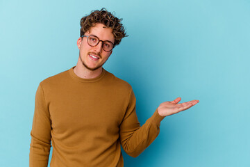 Young caucasian man wearing eyeglasses isolated on blue background showing a copy space on a palm...
