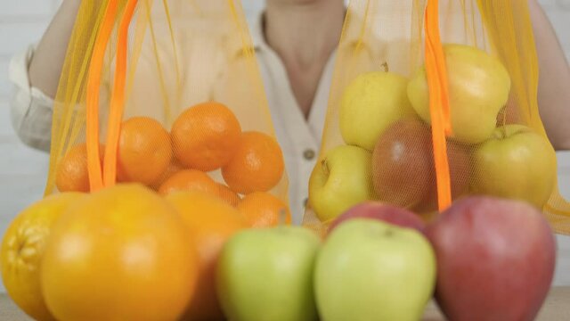 Woman hold eco fruits. A female hold two eco shoppers with fruits by the table in the room.