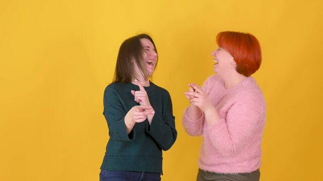 Two young girl pointing finger at camera and laughing out loud isolated on yellow background. female with funny face enjoy positive emotions screaming with laughter.