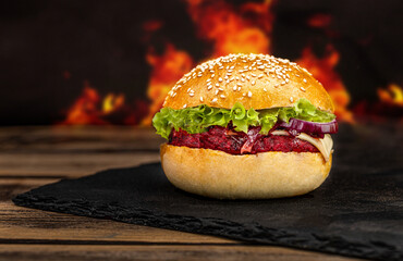 Tasty street food grilled vegetarian beetroot burger in crispy bun with lettuce and avocado on black stone board.