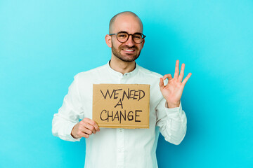 Young caucasian bald man holding a We need a change placard isolated on purple background cheerful and confident showing ok gesture.