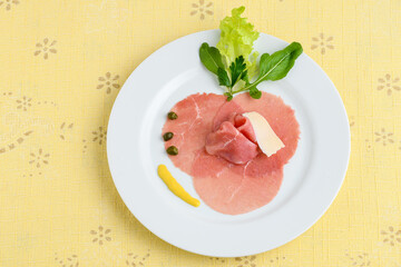 carpaccio on a white plate on a yellow tablecloth