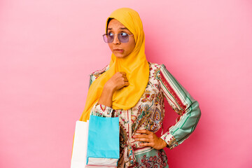 Young muslim woman shopping some clothes isolated on pink background confused, feels doubtful and unsure.