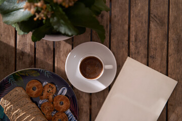 top view, holding coffee cup with wooden background, flowers, books and snacks 