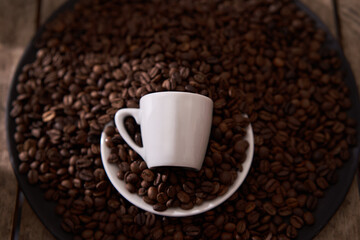 top view, white coffee cup, raw and roasted coffee beans in the dark plate on the wooden table