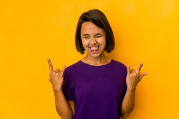 Young hispanic woman isolated on yellow showing a horns gesture as a revolution concept.
