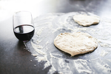 simple food ingredients, pizza dough and flour on kitchen bench ready for homemade pizza next to a glass of red wine