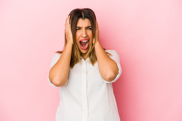 Young indian woman isolated on pink background covering ears with hands trying not to hear too loud sound.