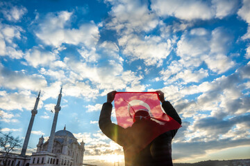 Man hold Turkish flag. Sunrise near Bosphorus bridge (aka: 15 July Martyrs Bridge Turkish: 15 Temmuz Sehitler Koprusu) and Imperial Mosque of Sultan Abdulmecid in Ortakoy, Istanbul, Turkey. Patriotism