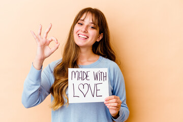 Fototapeta na wymiar Young caucasian woman holding a made with love placard isolated cheerful and confident showing ok gesture.