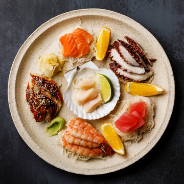 Sashimi sushi set with scallop on shell with daikon and lemon on plate on dark background